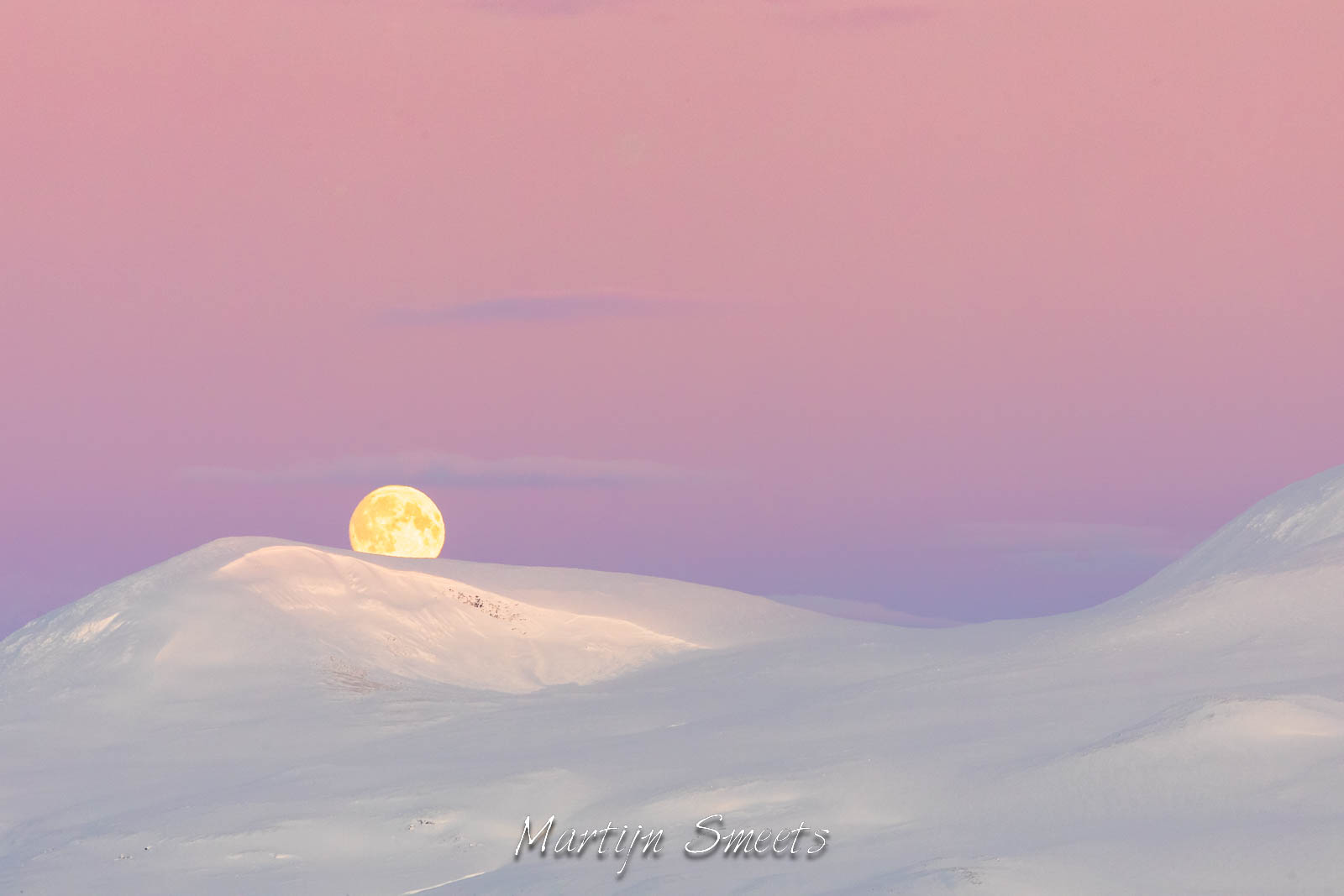 Full moon setting over the snowy mountains of Dividal in Norway.